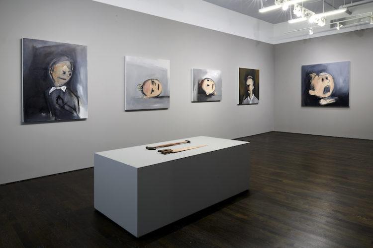 Five paintings installed on gray walls. In the foreground, two found object sculptures lie on a pedestal.